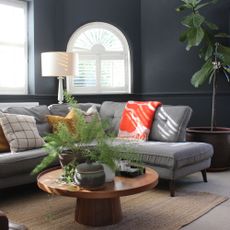 Corner of a black living room with grey chaise sofa and arched window
