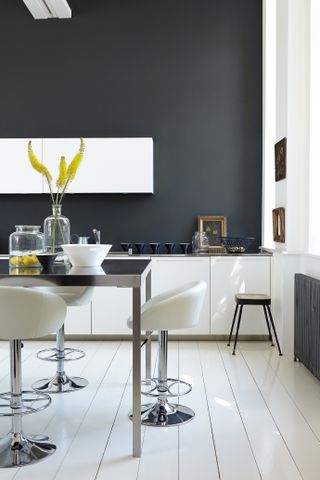 A kitchen with grey wall paint decor, white kitchen floorboards and white bar stools