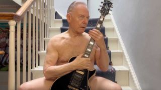Robert Fripp sitting naked on some stairs with a guitar