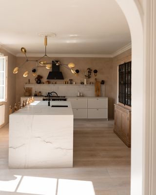 A kitchen with light pink limewash walls and brass fixtures