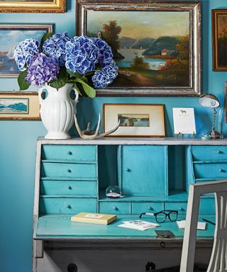 bedroom with blue walls and blue vintage desk, gray chair and artwork