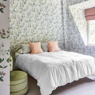 Bedroom with floral wallpaper on the walls and ceiling with white duvet cover and pink cushions and Roman blind