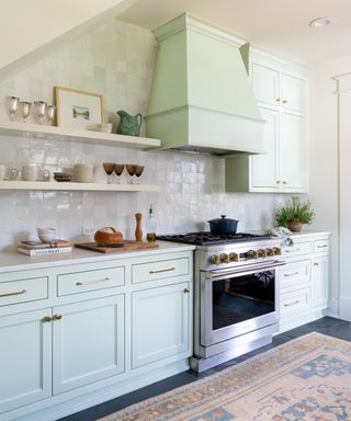 Kitchen with pale blue cabinets and green hood, range, tiled wall and rug on floor