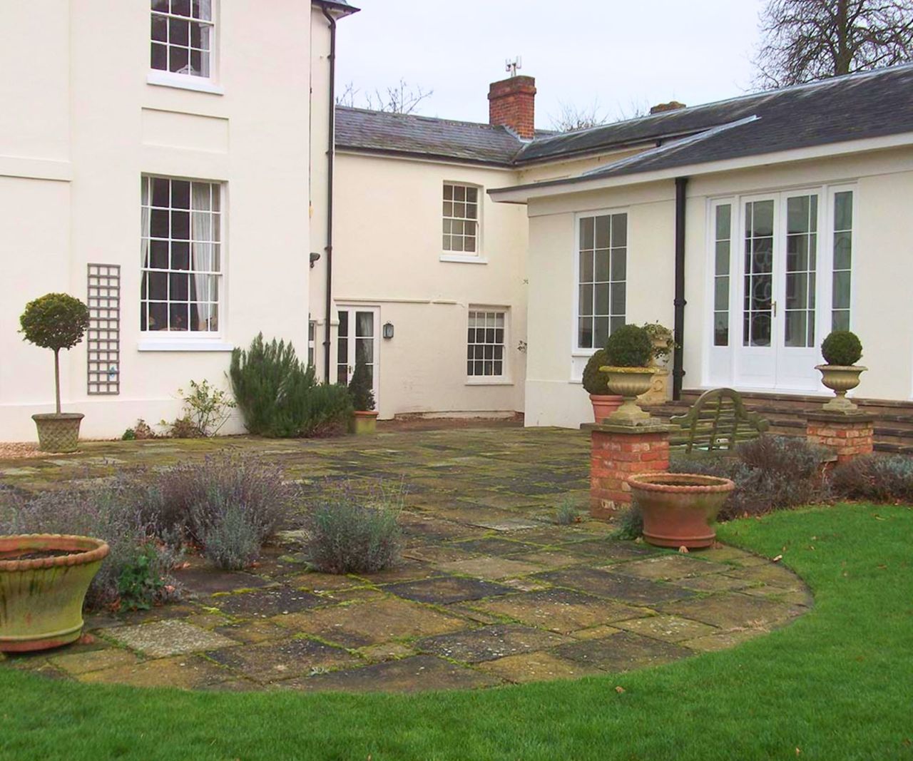 The rear of a white rendered Georgian country house with a low white-framed orangery wing, an old stone-paved courtyard with terracotta pots.