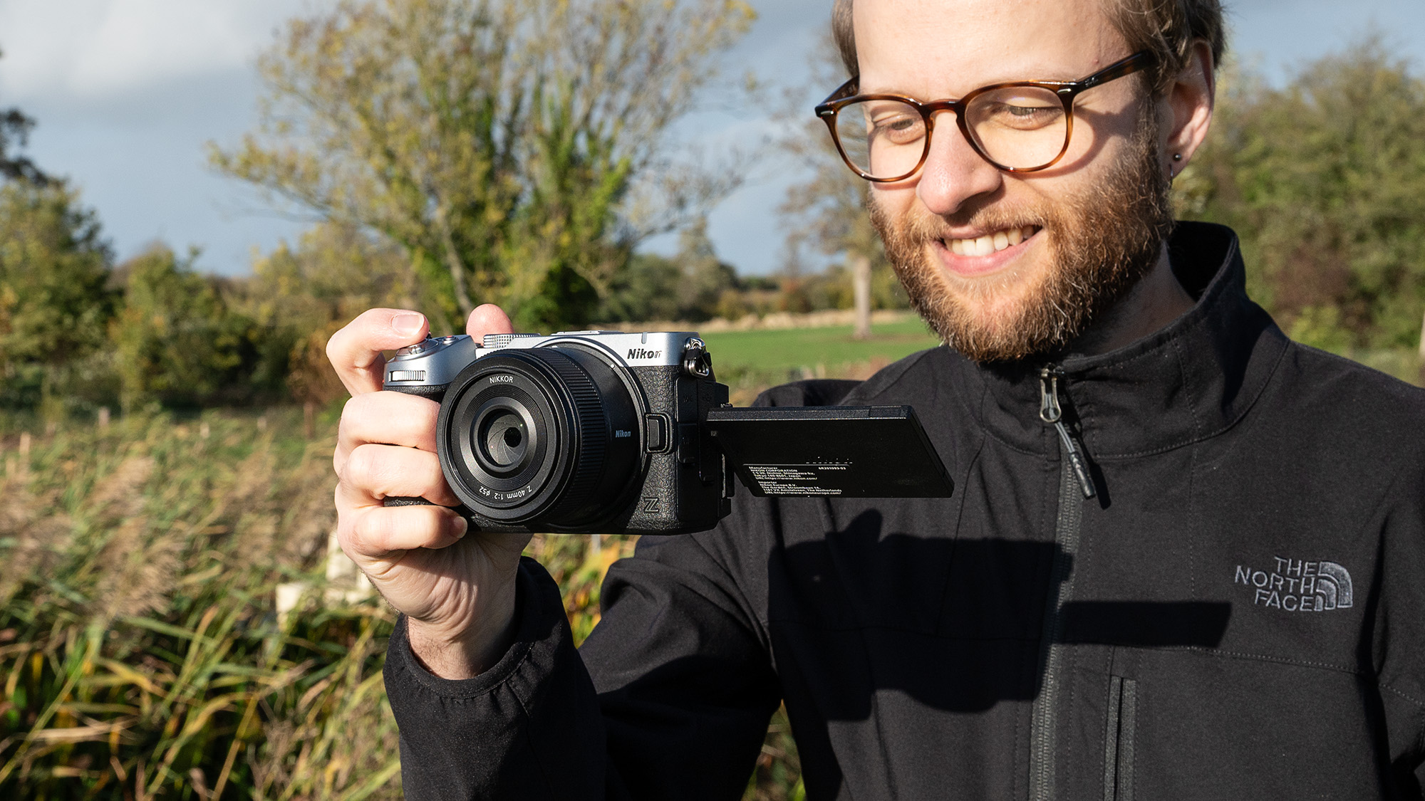Mike Harris wearing a black jacket holding the Nikon Z5IIC on a green background