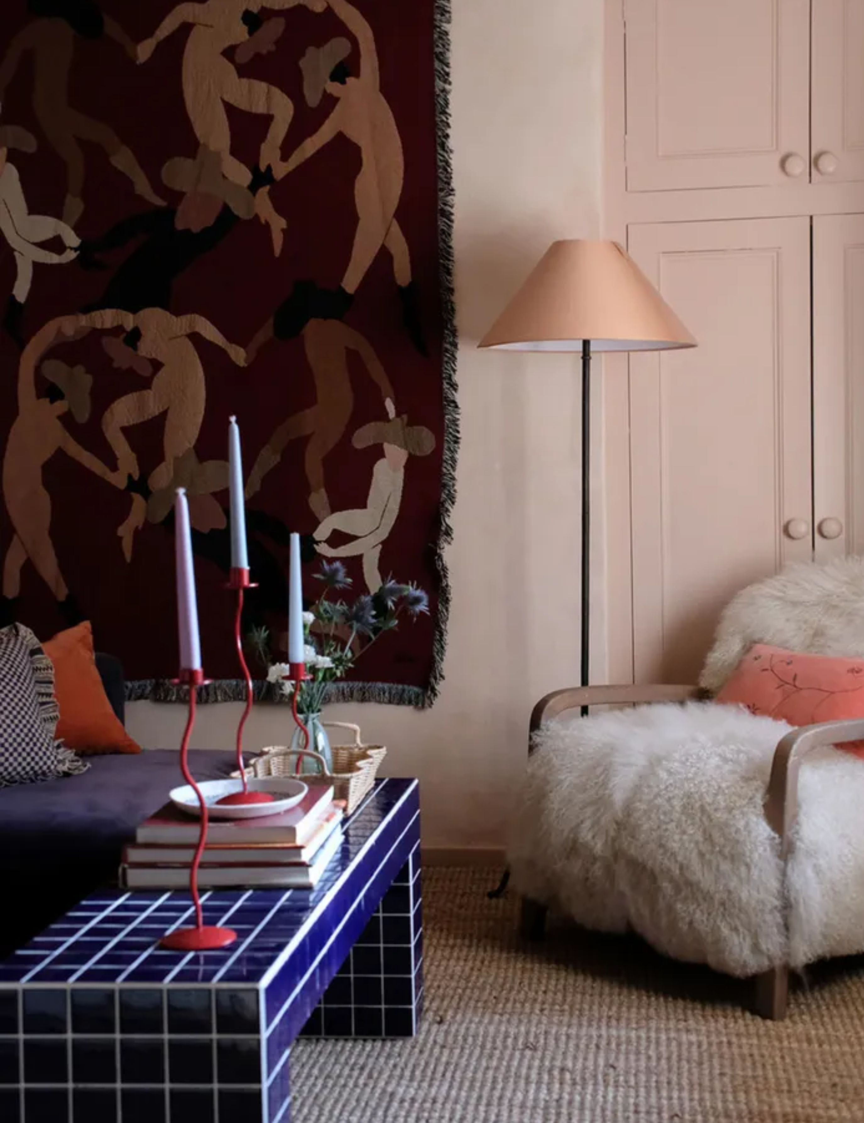Eclectic living room with pink cupboard, fluffy armchair and blue tiled coffee table and tapestry hanging