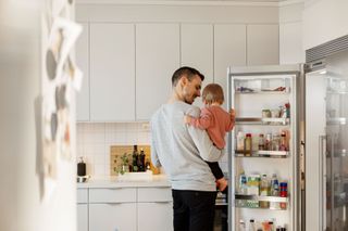 A father with a child looks into a fridge in the kitchen