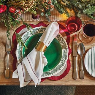 white Christmas napkin folded and ties with gold leaf cut-out and placed on dinnerware next to red glass