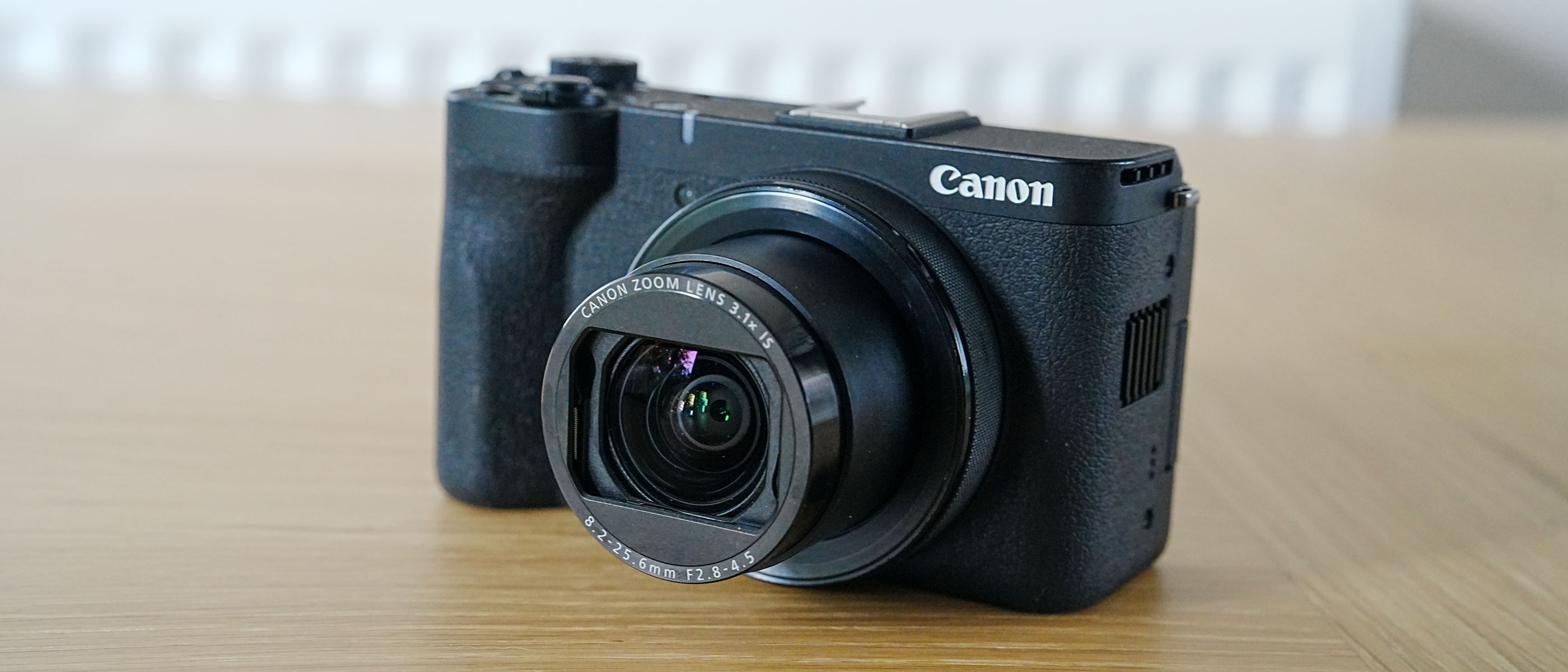 A Canon Powershot V1 with shutter open on a wooden table.
