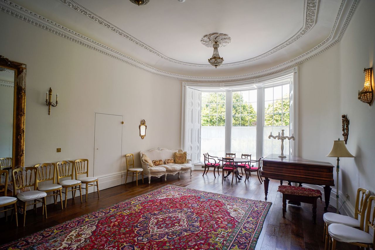 A music room inside the mansion with red rug and large floor to ceiling windows