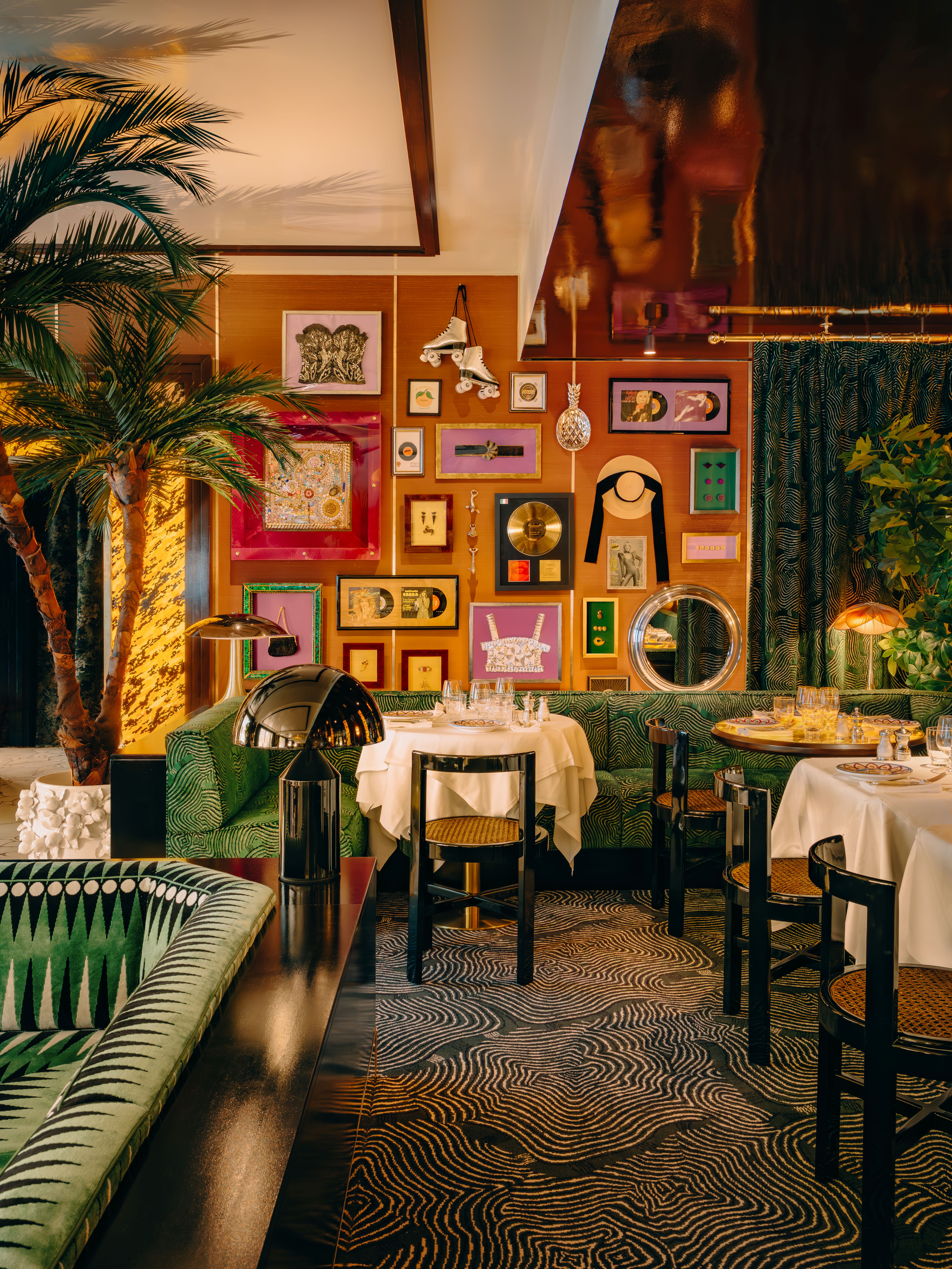 A cafe with burnt orange walls covered in framed vinyls and movie props, with green banquettes and palm trees
