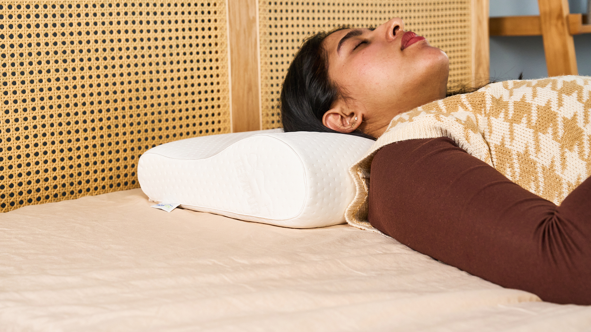 Woman sleeping on the Tempur-Neck white curved pillow against a rattan headboard