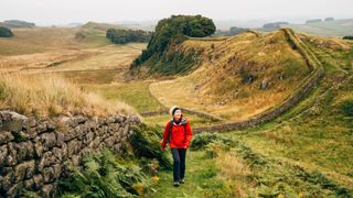 Woman walking in red hiking jacket and activewear across Hadrian's Wall in Scotland