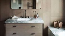 gray and beige bathroom with timber panelling on walls and vanity, gray marble countertop and built-in bath, black hardware, and wall-mounted mirror