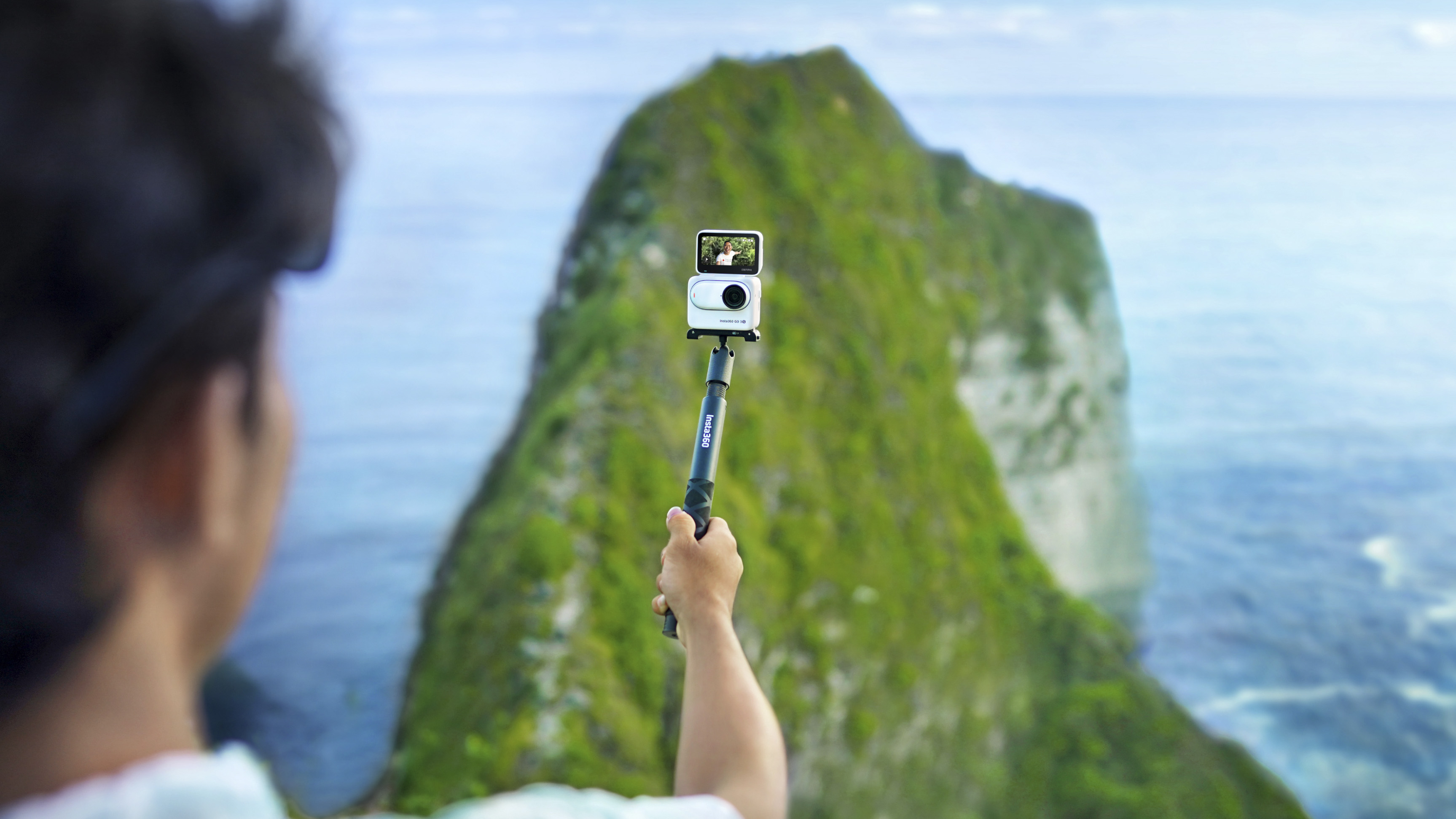 Insta360 Go 3S camera in the Action Pod and attached to a selfie stick with ocean backdrop