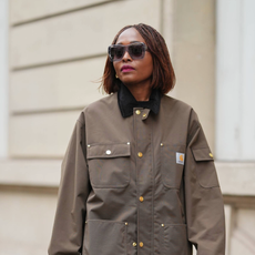 PARIS, FRANCE - DECEMBER 13: Carrole Sagba wears a straight chin-length bob hairstyle with a center part, makeup featuring a natural complexion with soft pink lipstick, an olive green khaki cotton canvas workwear jacket with flap chest pockets and snap-button fastening by Carhartt, black opaque tights, a burgundy leather tote bag with a structured silhouette and crocodile pattern, and burgundy shiny knee-high leather boots with a pointed toe and block heel and crocodile pattern, during a street style fashion photo session, on December 13, 2025 in Paris, France. (Photo by Edward Berthelot/Getty Images)