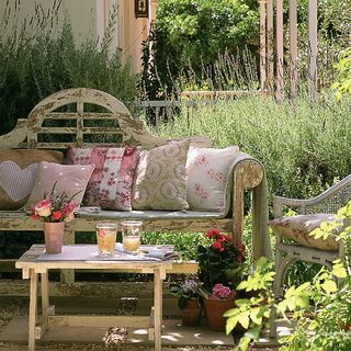 Country-style garden with wooden bench, table and pink-hued cushions