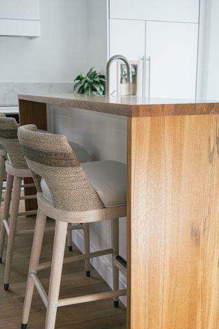 A wooden kitchen island with wooden waterfall worktop and gray barstools