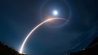 A rocket launch carves an orange arc into a dark night sky in this long-exposure photo.