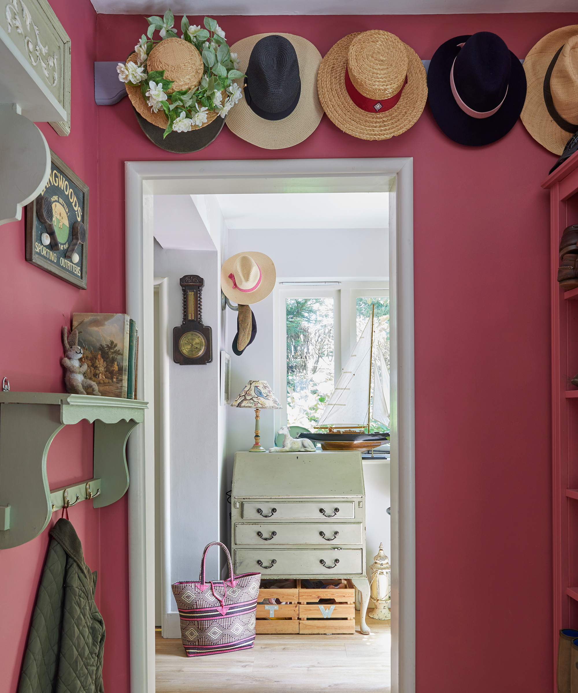 A red painted cloakroom with wall hat display and view through to hallway and vintage bureau