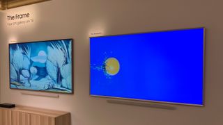 Two Samsung lifestyle TVs, The Frame and The Frame Pro, hanging on a beige-colored wall next to one another while displaying blue-colored artwork