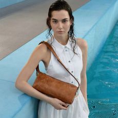 Woman standing in pool in white dress with wet hair, wearing tan Charles & Keith bag 