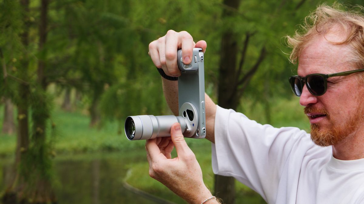 Tim Coleman, TechRadar's Cameras Editor, holding the Vivo X500 Pro Max phone with teleconverter lens attached, while stood on a wooden walkway in a birdlife reserve in Shanghai, China