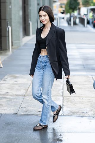 Lily Collins mengenakan blazer hitam, jeans, dan balerina Alaia