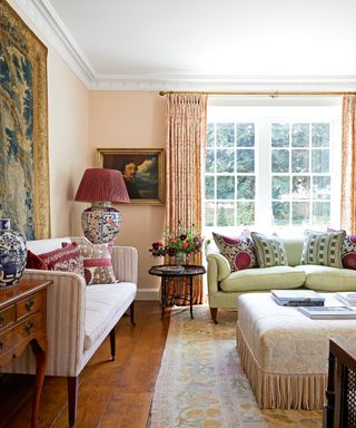 colorful living room with patterned cushions, curtains and rug, pink walls, green sofa, pink striped sofa and fringed ottoman