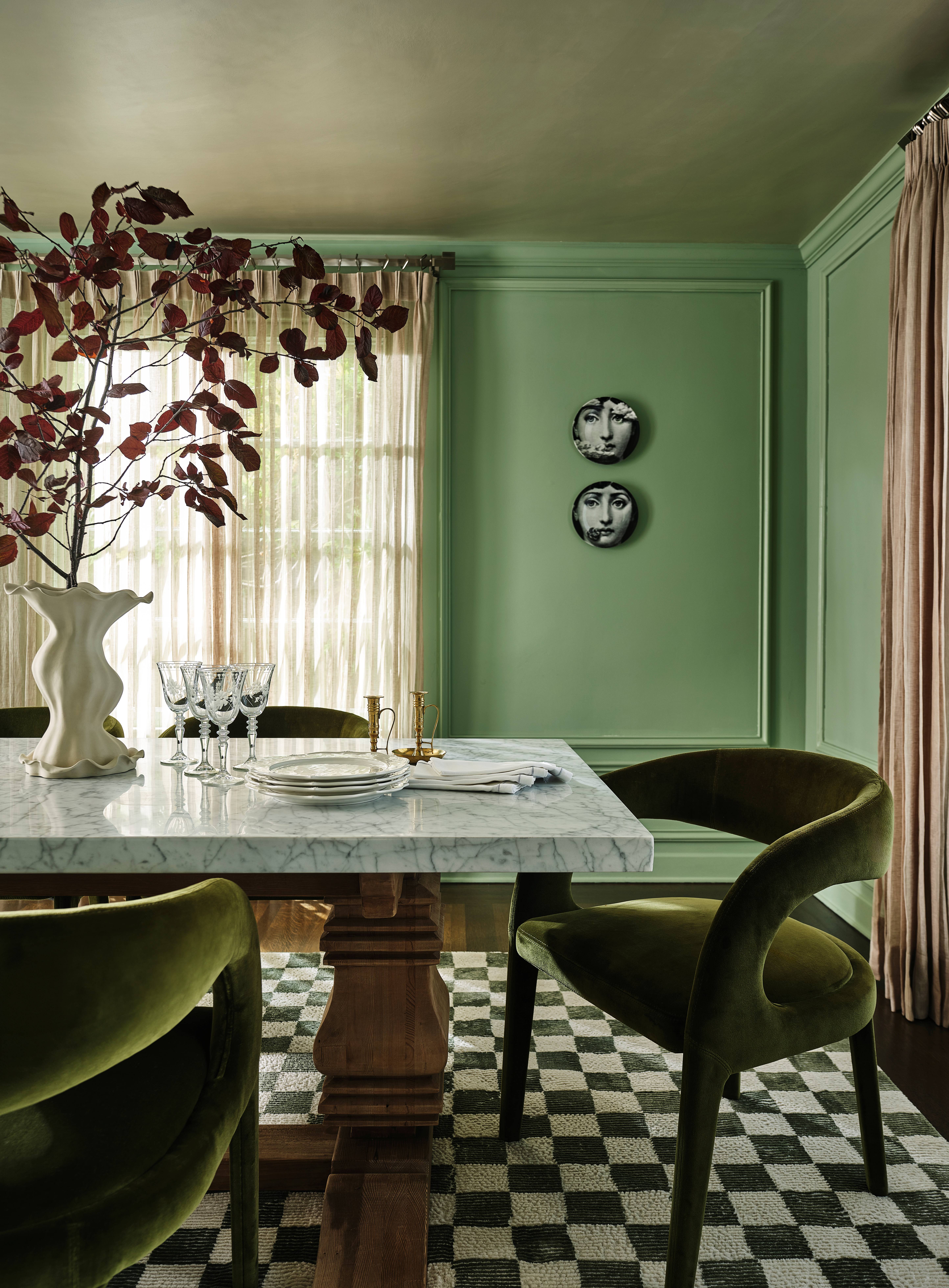 Tudor dining room by Atelier Oleana featuring green walls and chairs, a double pedestal dining table, and a checkered rug underneath.