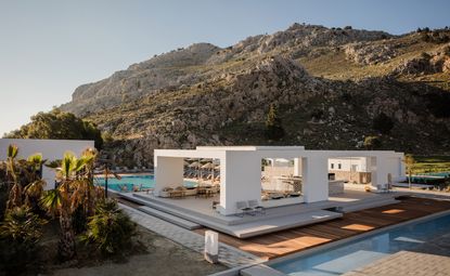 Sitting area with bar, chairs, wooden deck and a pool on either side with a view of the hillside.