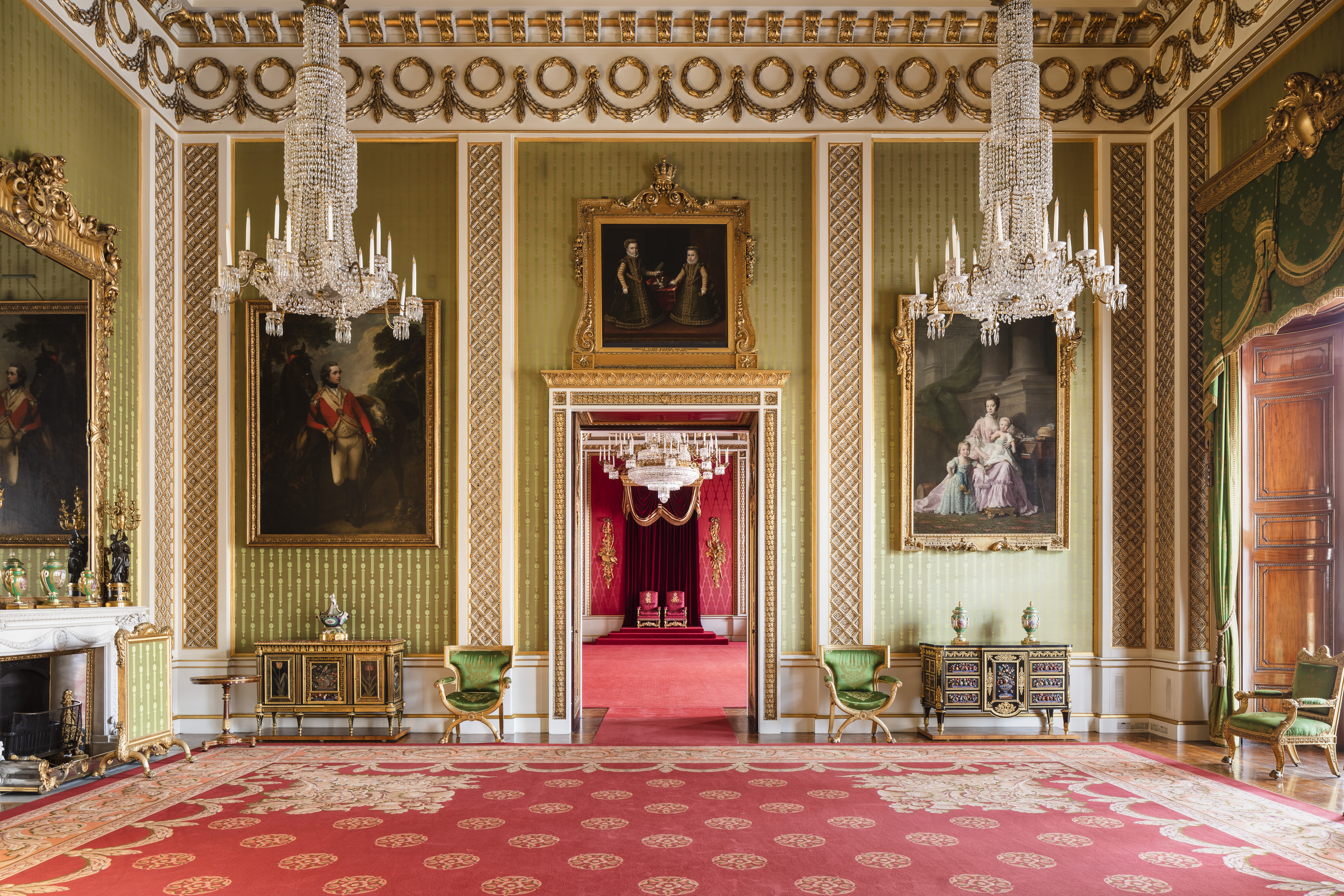 Green double height room with red carpet and large chandeliers, inside Buckingham Palace
