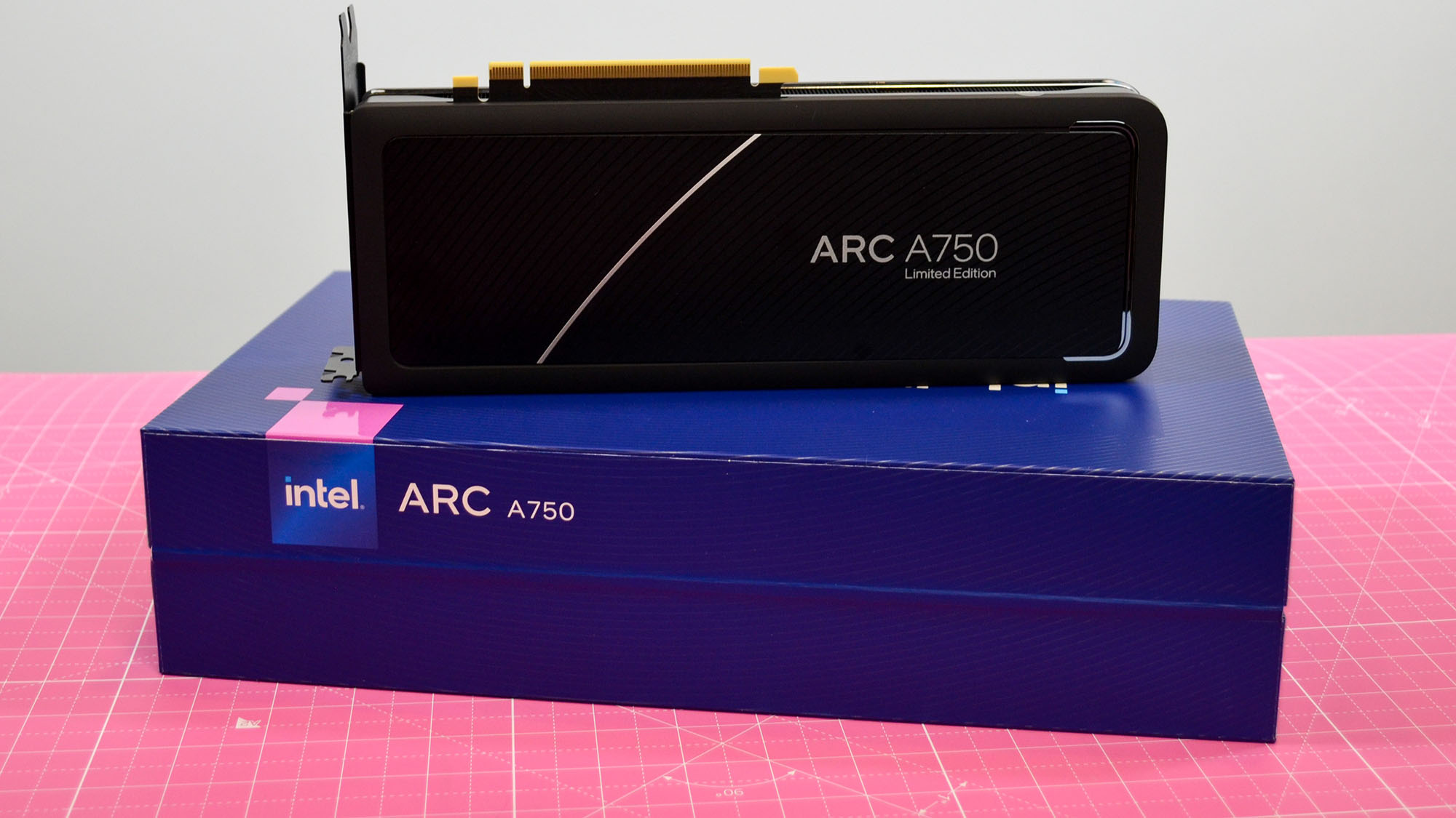 Uma placa gráfica Intel Arc A750 em um tapete de mesa rosa ao lado de sua embalagem retrátil