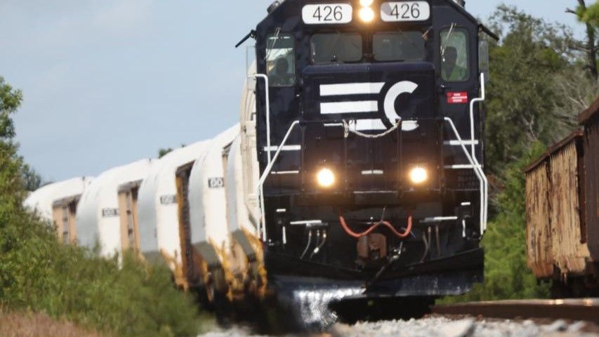 Train cars carry white cylinders on tracks