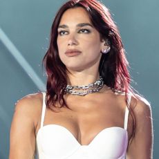 Dua Lipa stands on a stage wearing a white bra and Tiffany link necklaces in a stack