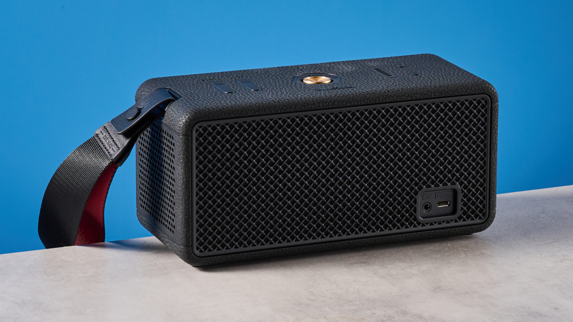 The Marshall Middleton II Bluetooth speaker in Black and Brass, on a stone surface with a blue wall in the background