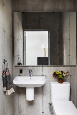 A modern powder room with cement walls and large mirror
