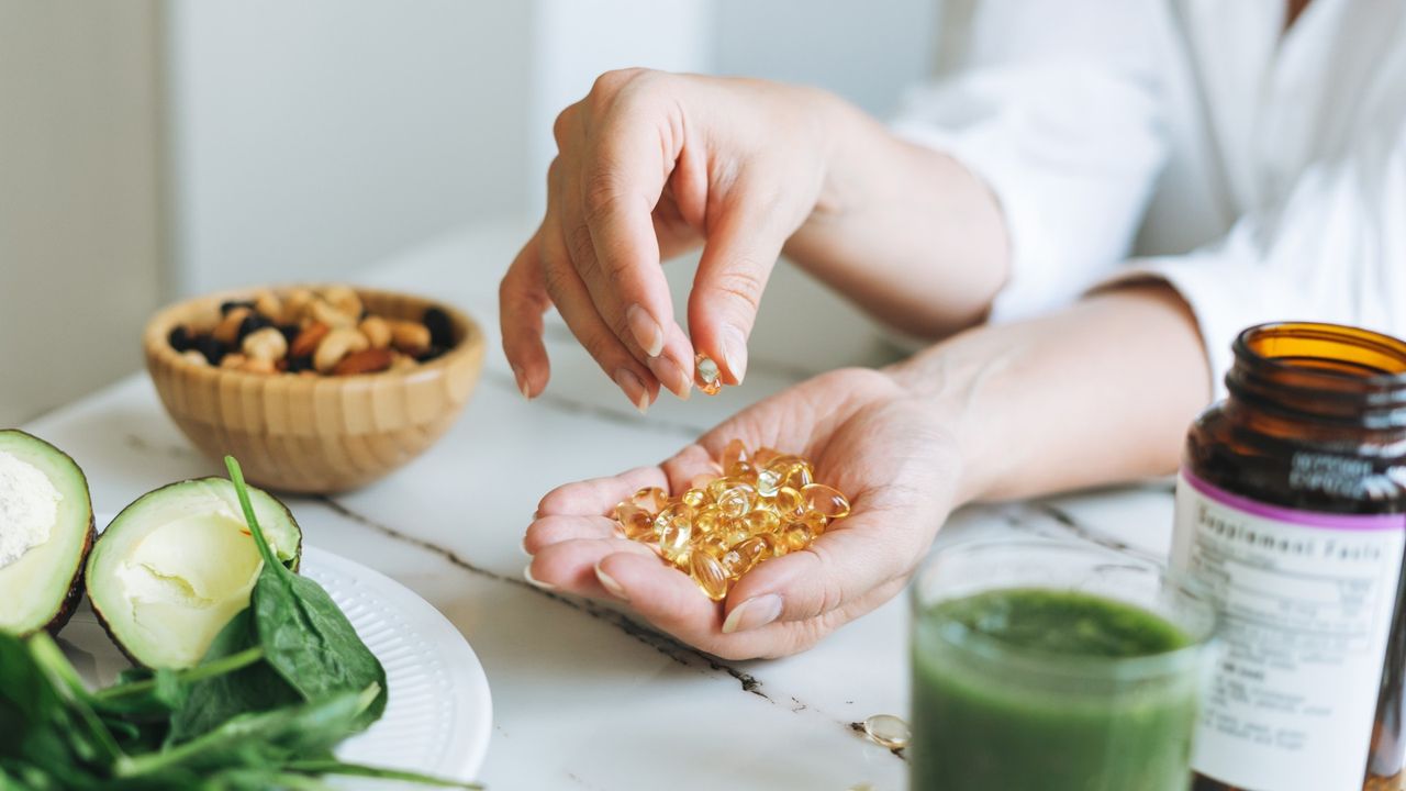 Woman&#039;s hand holding supplements at table 