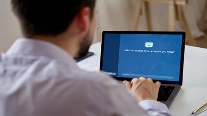 Back view of crop anonymous male talking to a chatbot of computer while sitting at home