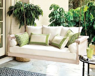 A cream porch swing hung with chains with green outdoor cushion decor