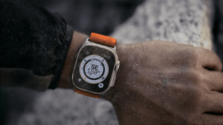 A person wearing an Apple Watch Ultra with an orange strap.