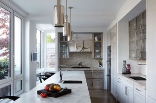A kitchen with white marble countertops, statement cylindrical lighting and chrome finishes