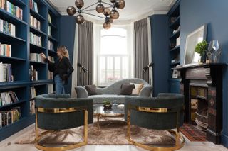 Bookcases and alcove shelving painted in deep blue. Gold-blue chairs and a chaise sofa
