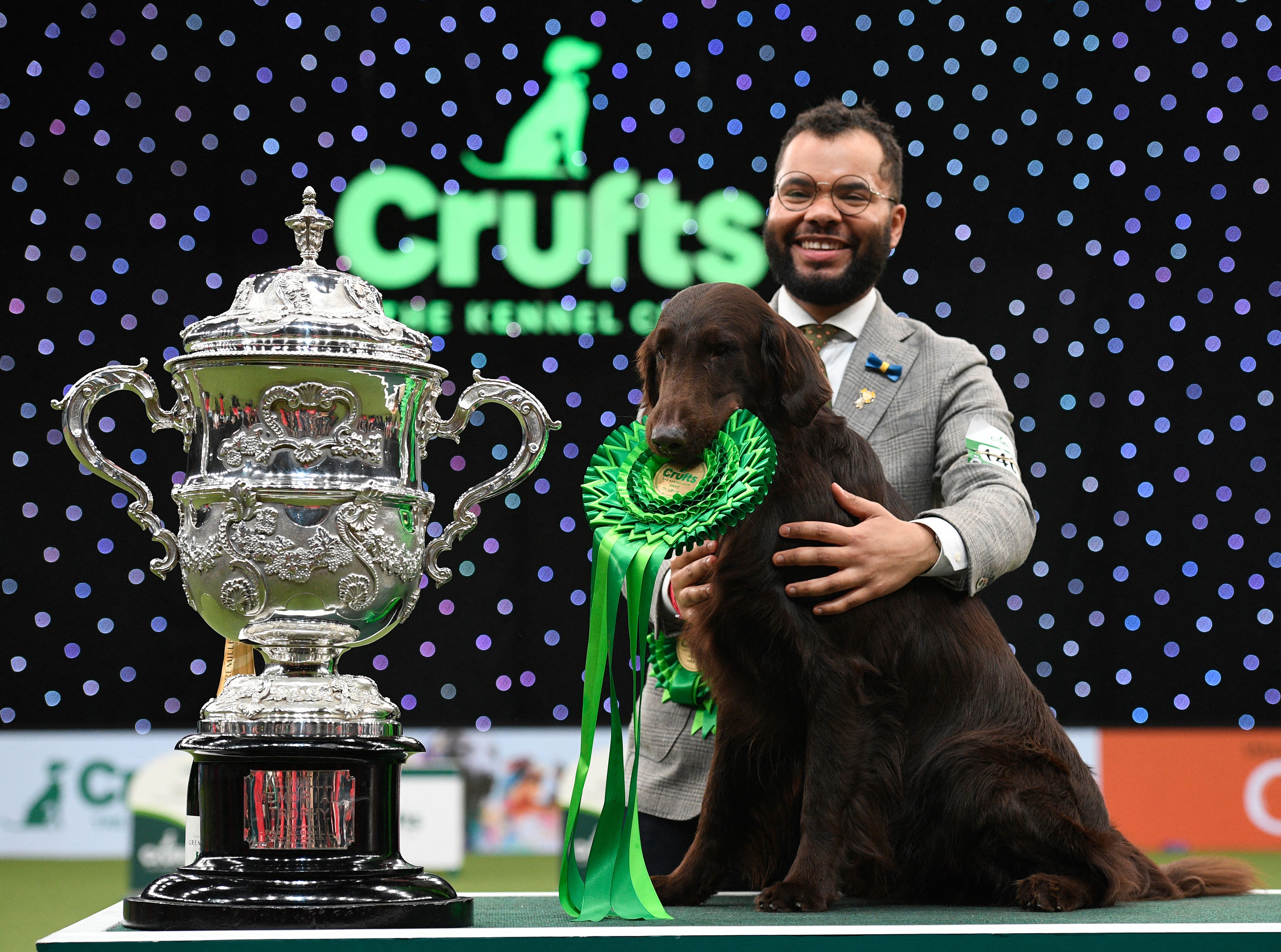 Flat-coated retriever Almanza Backseat Driver with handler Mr J P Oware and the Crufts Best in Show trophy at the NEC in Birmingham, 2022.
