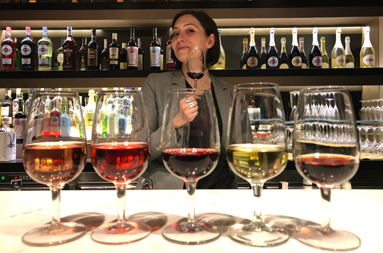 Five glasses of vermouth in front of a woman standing at a bar