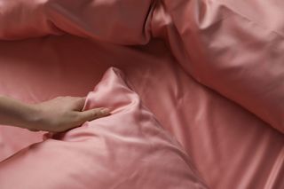 A woman's hand touching pink silk bedding