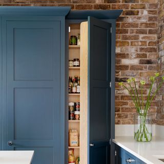 kitchen pantry with blue cupboard and exposed brick walls