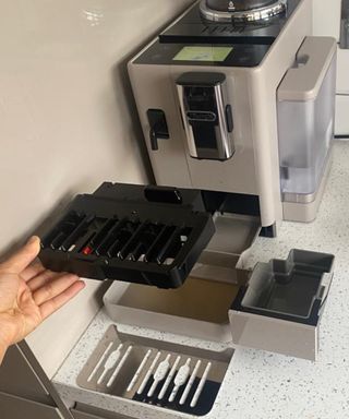 Christina Chrysostomou demonstrating how to remove drip tray and waste bin from De'Longhi Rivelia coffee maker for cleaning