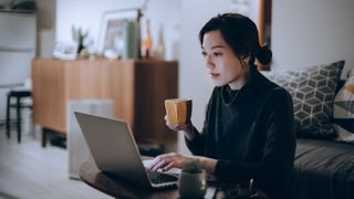 Woman holding mug while working on her laptop