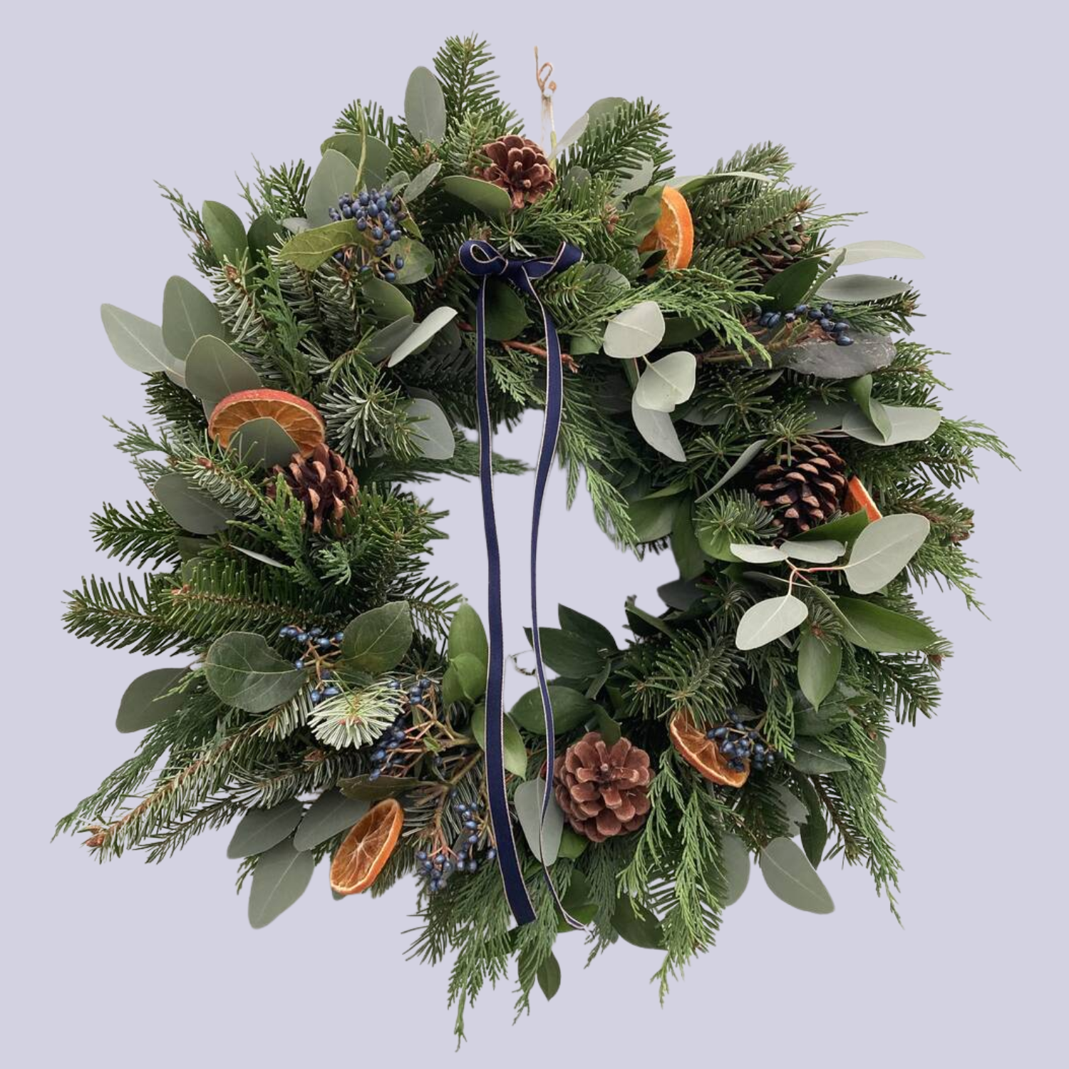 A green wreath with pinecones and dried orange slices with a blue ribbon